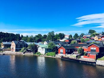 Houses by river and buildings against blue sky
