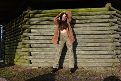 A young woman with a brown coat, posing in front of old wooden planks