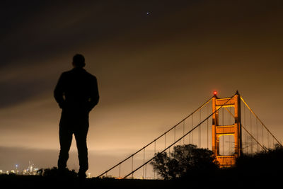 Silhouette man standing against golden gate bridge at night