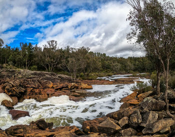 Stream flowing through rocks in river against sky