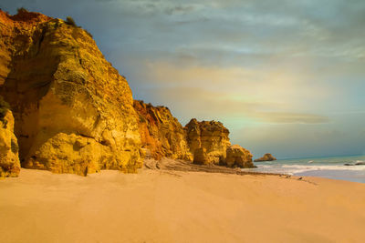 Rock formations on beach against sky during sunset