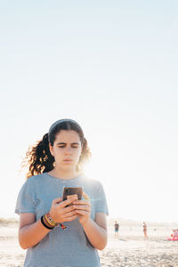 Young woman using mobile phone at beach against clear sky