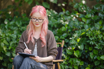 Portrait of young woman sitting against plants