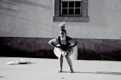 Portrait of woman dancing on footpath against wall