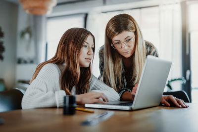 Mother assisting daughter in using laptop on table at home