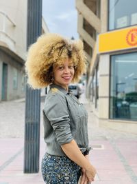 Portrait of smiling young woman standing against city