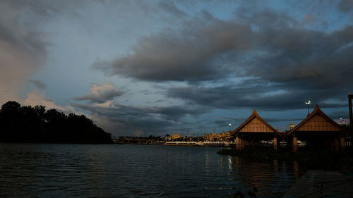 Houses by lake and buildings against sky at dusk