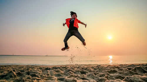 Man jumping on beach against sky during sunset