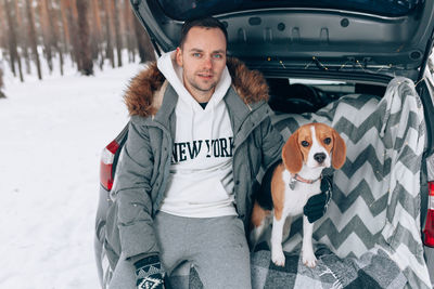 Portrait of man with dog sitting in car trunk during forest