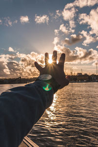 Midsection of person hand against sky during sunset