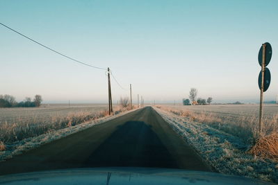 Street amidst field against sky seen through windshield