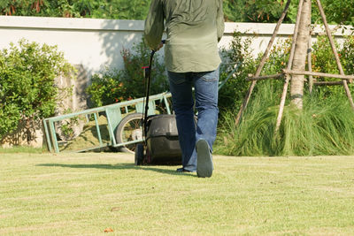 Back portrait gardener pushing the mowing cart on the grass field