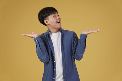 Young man looking away while standing against yellow background