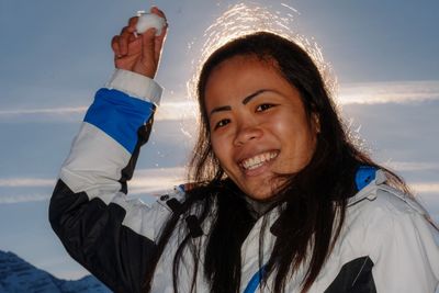 Portrait of smiling young woman holding snow standing against sky