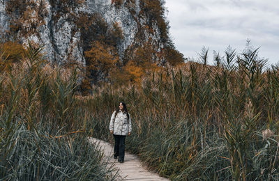 Front view of young adult woman walking on wooden path in forest in autumn.