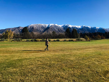 Person walking on golf course against clear blue sky