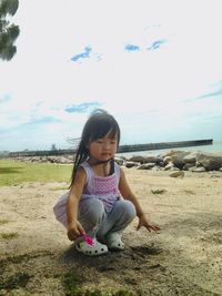 Cute girl sitting on land by sea against sky