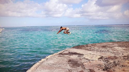 Shirtless man jumping in sea against cloudy sky