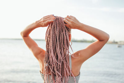 Rear view of woman with hand in hair standing at beach against sky