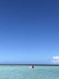 Rear view of woman standing with baby in inflatable pool raft at sea against sky
