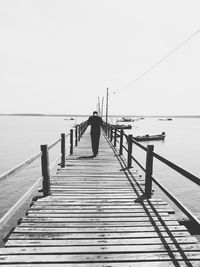 Man walking on pier over sea against clear sky