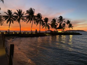 Silhouette palm trees by seashore against sky during sunset