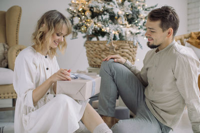 Man looking at girlfriend opening gift at home