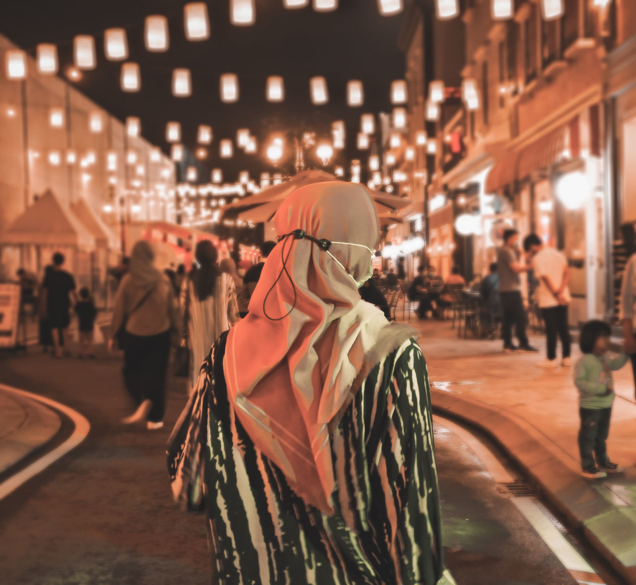 REAR VIEW OF PEOPLE WALKING ON ILLUMINATED STREET