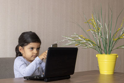 Cute girl using phone while sitting on table at home