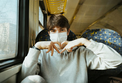 Portrait of a young man sitting in a train with a medical face mask during the covid-19 pandemic