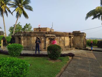 People by palm trees and building against clear sky