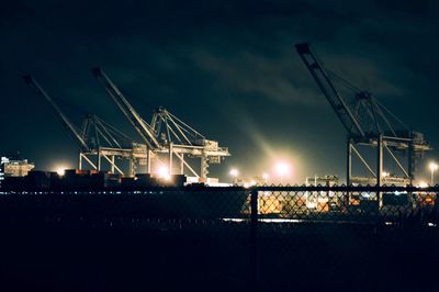 Illuminated cranes against sky at night