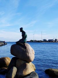 Statue on rock by sea against blue sky