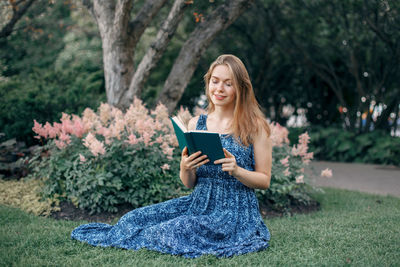 Smiling young woman reading book while sitting on field