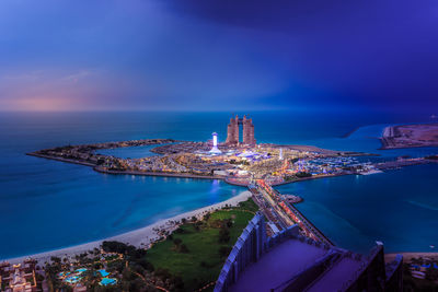 High angle view of illuminated city by sea against sky