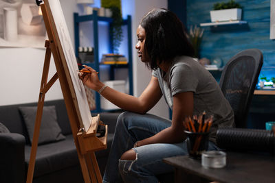 Side view of young woman sitting on chair at home