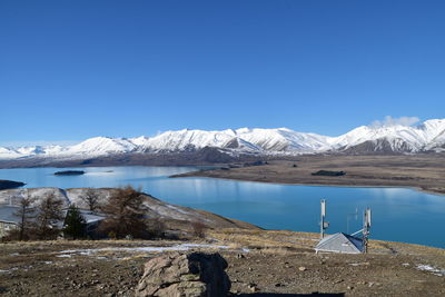 Scenic view of lake by snowcapped mountains against clear blue sky