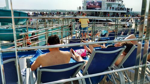 Rear view of shirtless man sitting on railing against sea