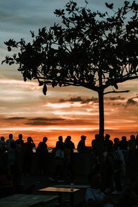 Silhouette people sitting by tree against sky during sunset