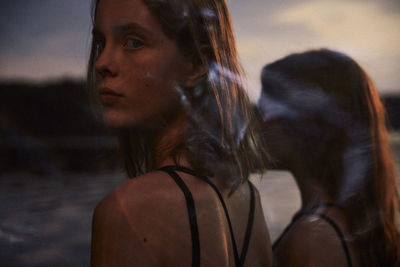 Close-up portrait of young women standing at beach during sunset