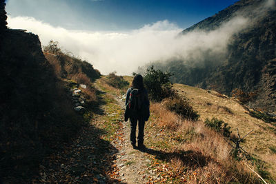 Rear view of woman hiking on footpath against sky