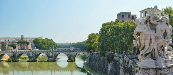 Statues by arch bridge over river at castel sant angelo against clear sky