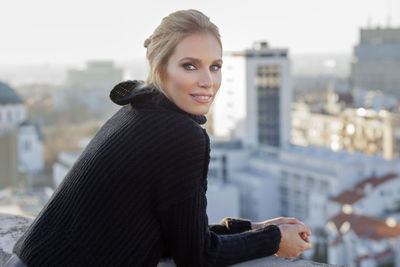 Side view portrait of woman leaning on retaining wall against city