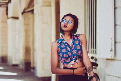 Young woman wearing sunglasses while standing by building