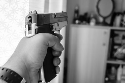 Cropped hand holding handgun against curtain