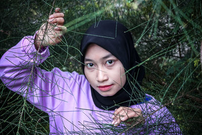 Portrait of young woman holding sunglasses against trees