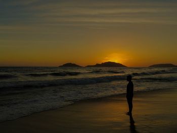 Silhouette man walking on beach against sky during sunset