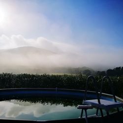 Swimming pool by lake against sky