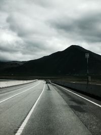 Empty road leading towards mountains against cloudy sky