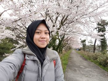 Portrait of smiling young woman standing by cherry tree